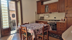 Cozinha com armários de madeira, uma mesa de jantar com toalha florida e vista através de uma porta de vidro.