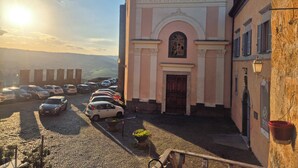Uma igreja com fachada rosa, um pátio de pedra e carros estacionados, sob um céu limpo.