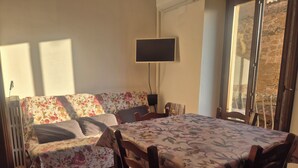 Quarto com sofá, mesa de jantar, televisão e janela.