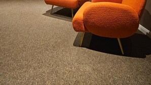 Ein Zimmer mit zwei orangefarbenen Sesseln, einem Fenster mit blauer Tönung und einem Teppichboden.