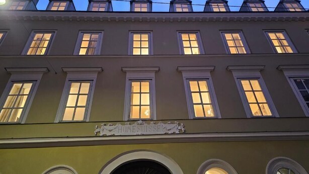 Ein mehrstöckiges Gebäude mit beleuchteten Fenstern und einem Schild mit der Aufschrift 'Homesuisse'.