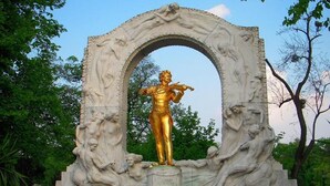 Eine Statue zeigt eine Person, die Geige spielt, umgeben von einem verzierten Steinbogen.