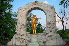 En statue af en figur, der spiller violin, omgivet af en detaljeret stenhvælv.
