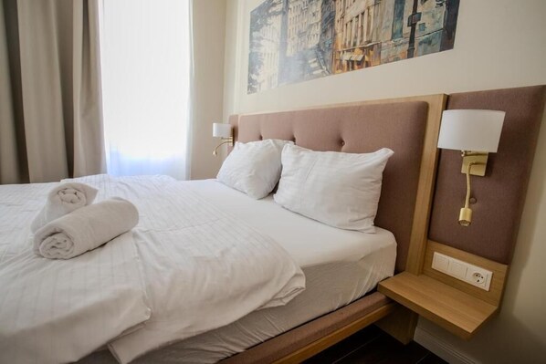 Un lit bien fait, avec du linge de lit et des serviettes blanches, une tête de lit dotée d’un luminaire et un tableau accroché au mur.