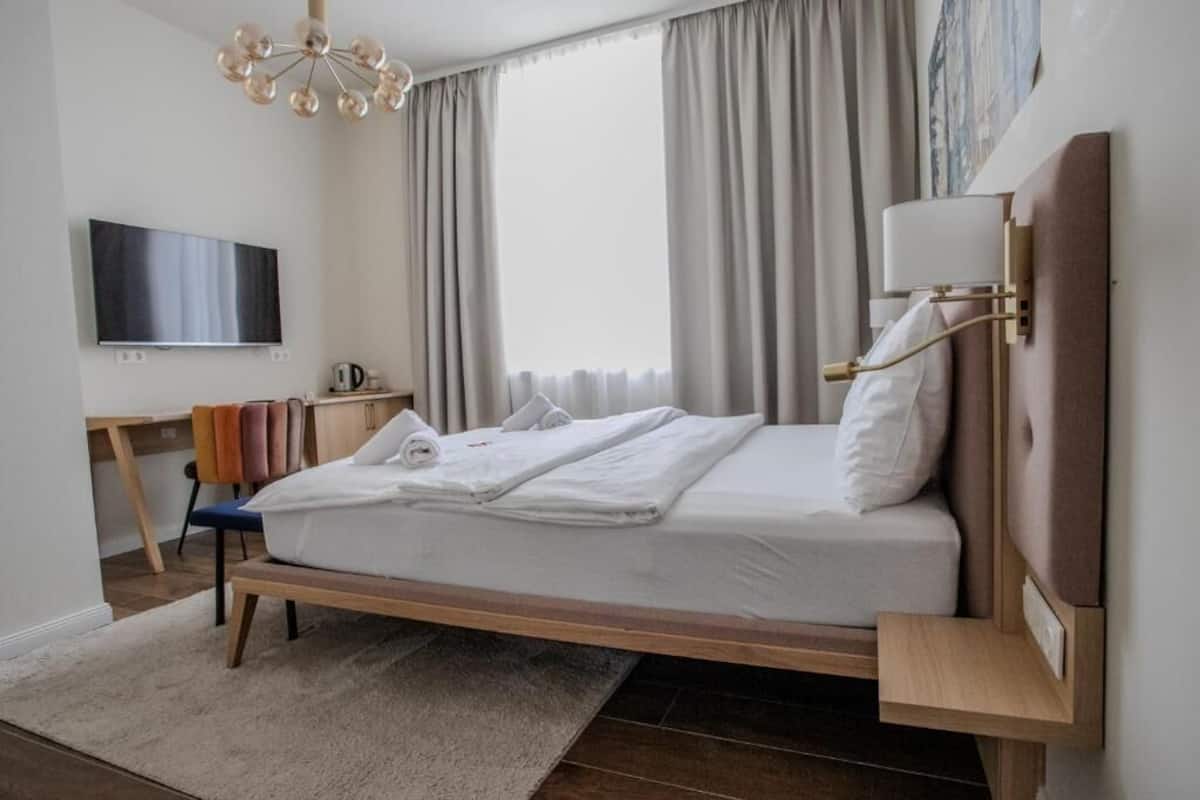 A modern hotel room with a bed, a TV, a desk, and a chair.