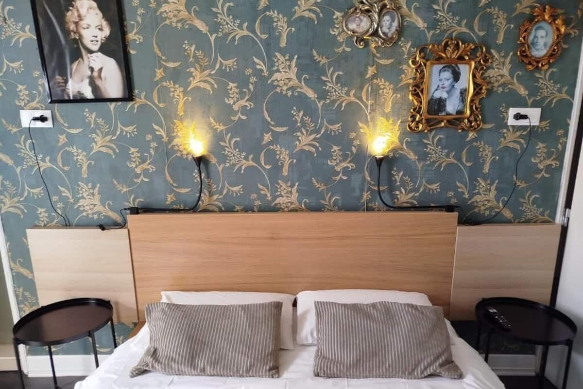 A hotel room with a bed, two bedside tables, a headboard, and wall-mounted picture frames.