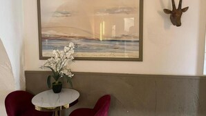 A room with a framed painting, a potted plant, a red chair, and a mounted animal head. - São Pedro Suítes (Faro)