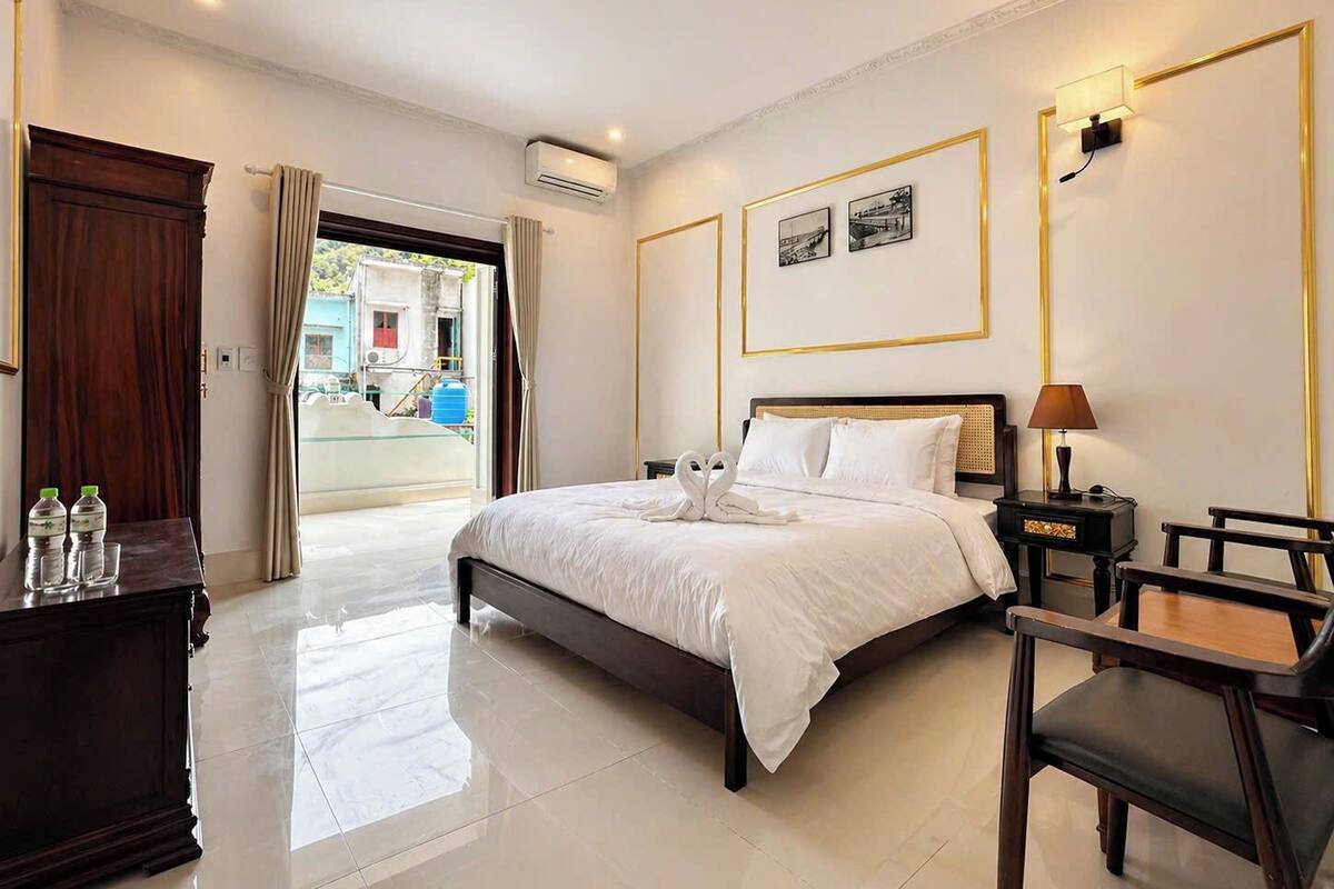 Una habitación de hotel con cama, mesita de noche, lámpara y vistas al exterior.