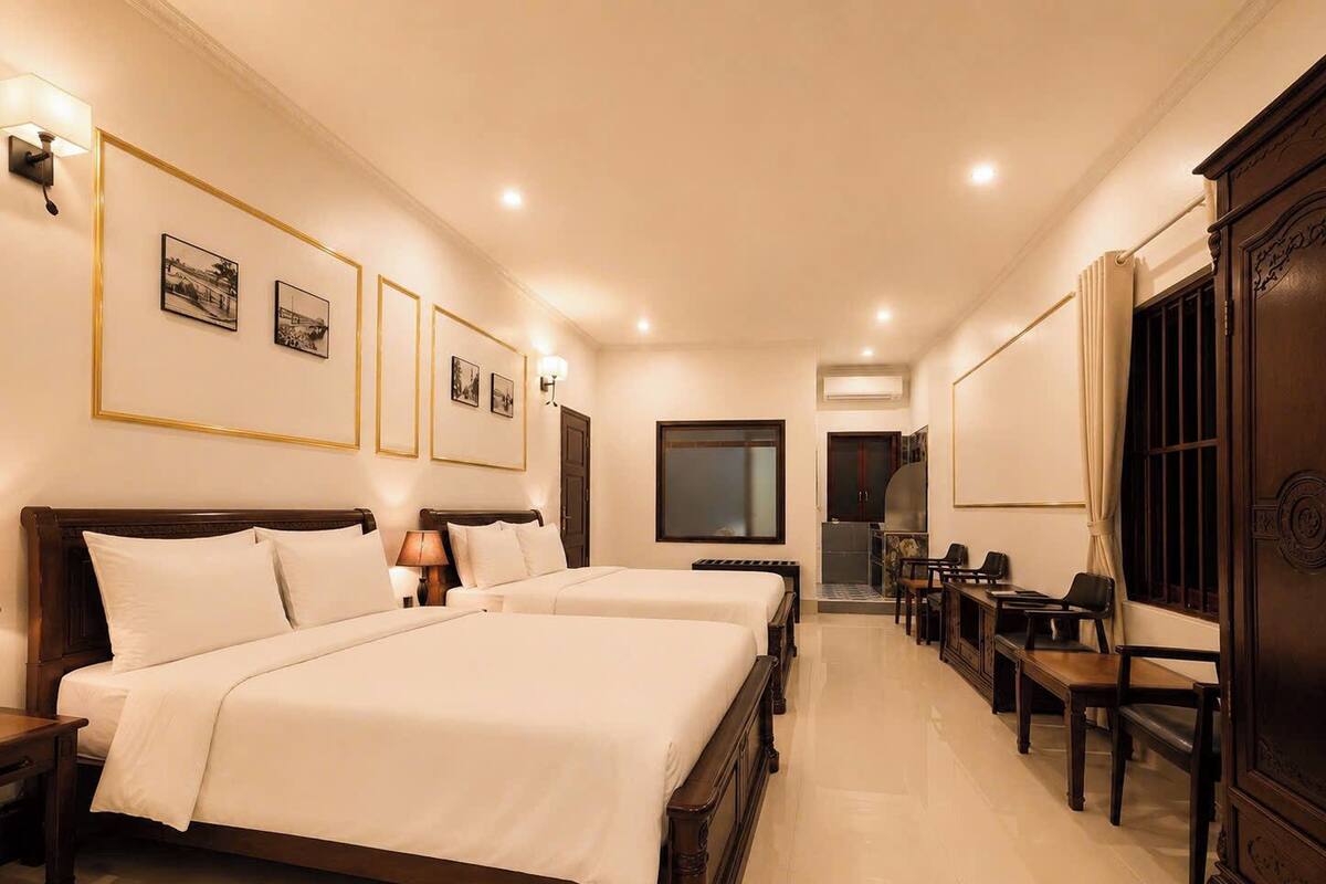Habitación de hotel con dos camas, un escritorio, sillas, un televisor y cuadros en la pared.