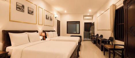A hotel room with two beds, a desk, chairs, a TV, and framed pictures on the wall.