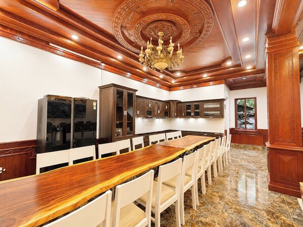 Una cocina amplia con una encimera de madera larga, sillas blancas y armarios de madera oscura.