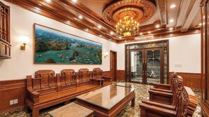 A conference room with a large wooden table, matching chairs, a chandelier, and a large landscape painting on the wall. - Rose Wood Cat Ba Villa (Hai Phong)