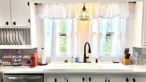Eine Küche mit weißer Arbeitsplatte, einem schwarzen Wasserhahn und einem Fenster mit transparenten Vorhängen.