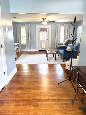 A living room with hardwood flooring, a ceiling fan, a blue sofa, a white armchair, a coffee table, and a side table. - The Cozy Cottage: 3-bedroom/2-bath home in the heart of Lucedale (Lucedale)