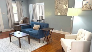 Ein Wohnzimmer mit blauem Sofa, weißem Sessel, Couchtisch und Lampe.
