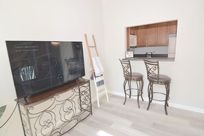 A modern kitchen with a flat-screen TV, two bar stools, and a wooden cabinet. - Coastal Getaway~Large Clean-n-Cozy 3Bdrm Home (Virginia Beach)