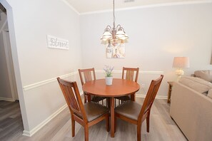 Un comedor con una mesa redonda de madera, cuatro sillas, una lámpara colgante y una planta en maceta.