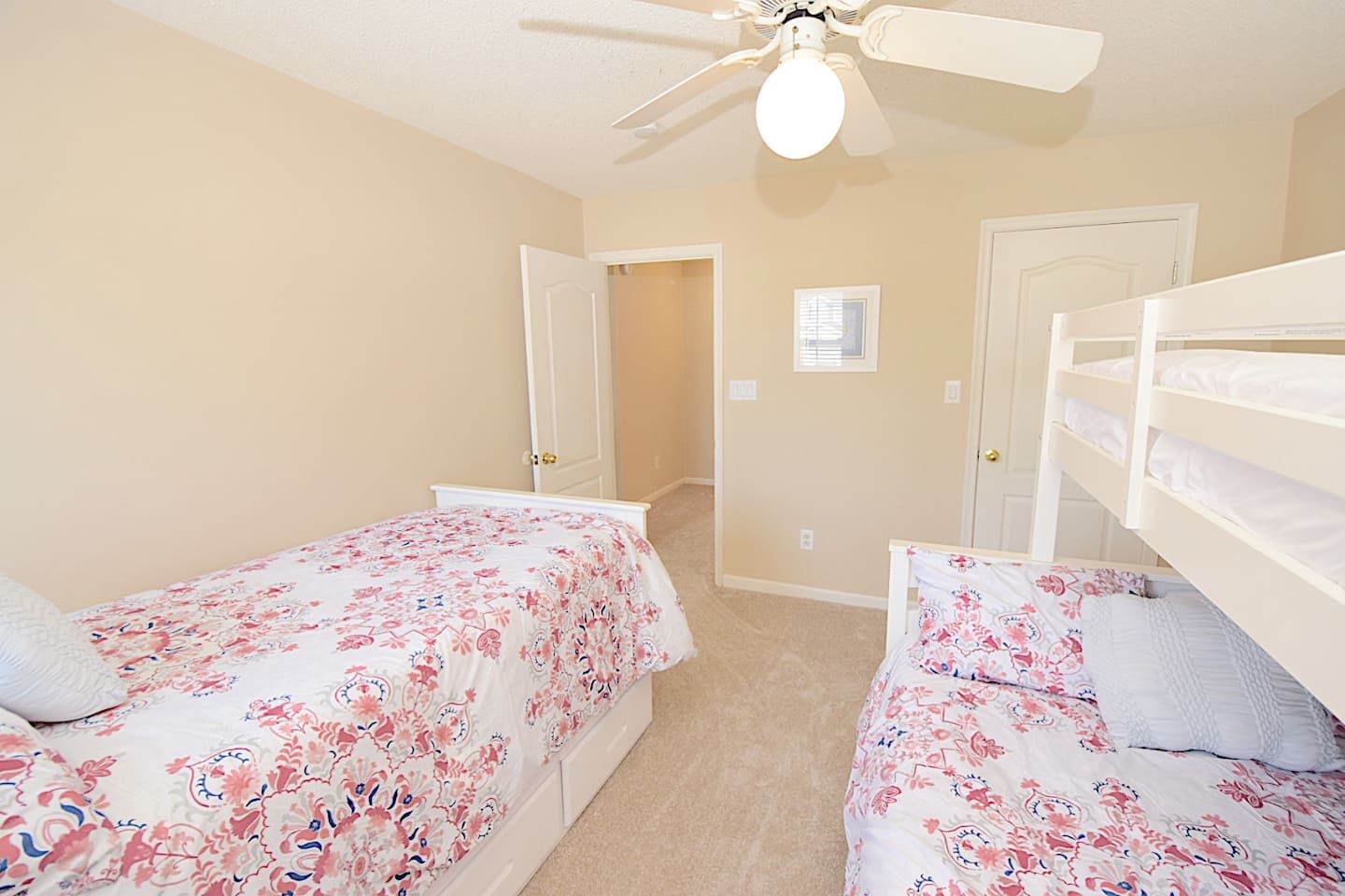 A bedroom with two single beds, a ceiling fan, and a door leading to another room.