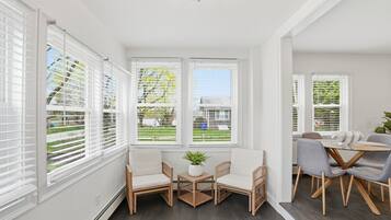 A bright room with large windows, wicker furniture, and a small table with a plant.