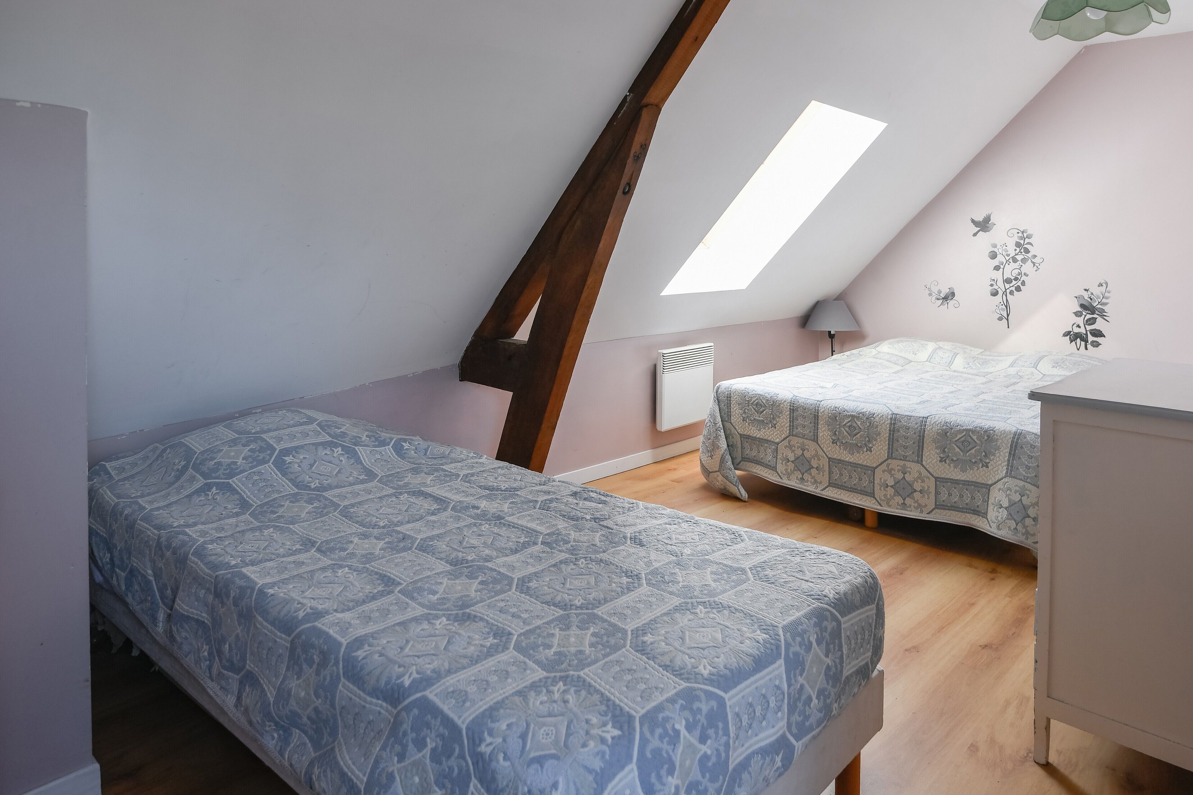 Une chambre avec un plafond en pente, deux lits, un radiateur et une fenêtre.