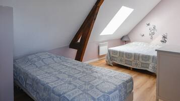 Une chambre avec un plafond en pente, deux lits, un radiateur et une fenêtre.