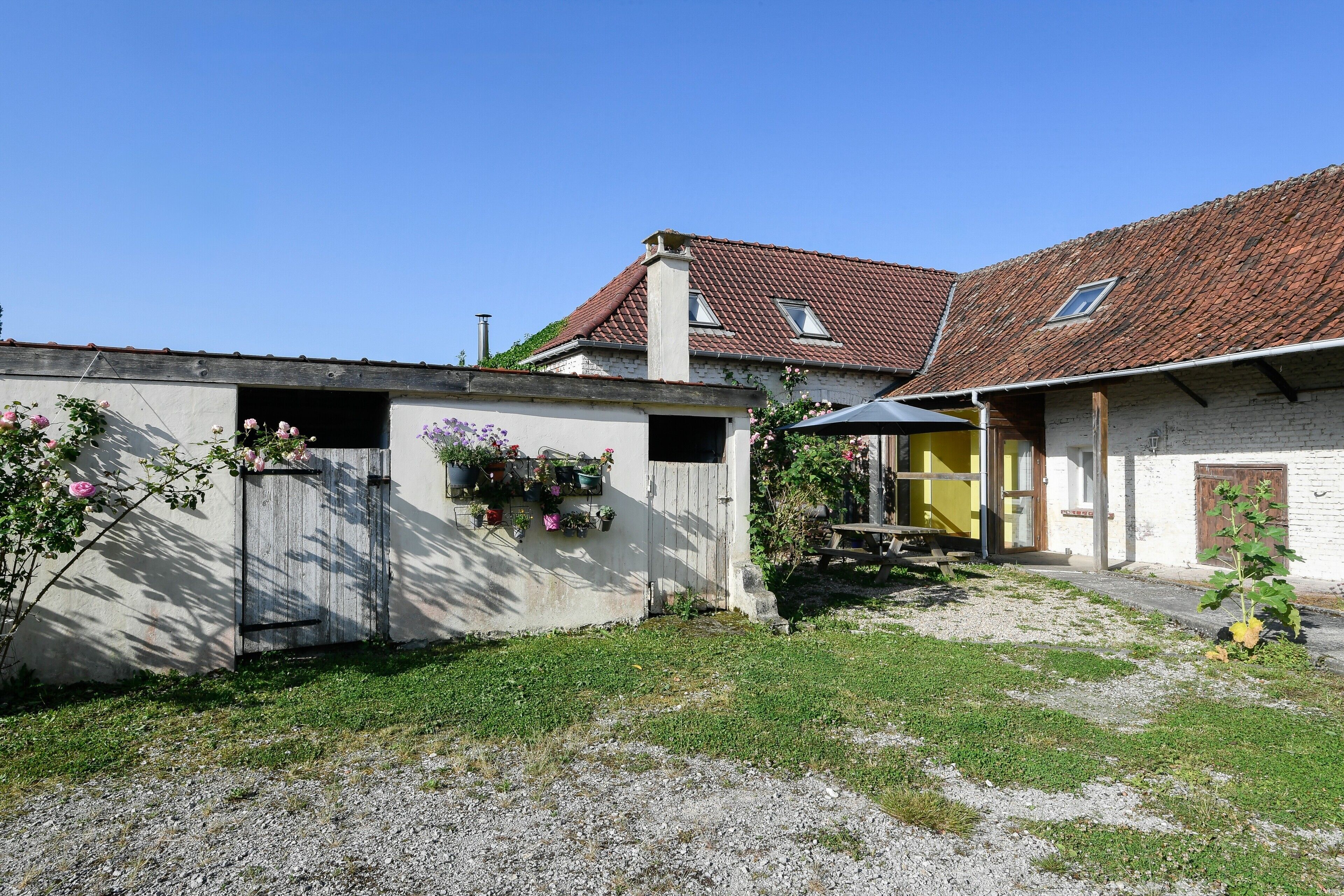 A two-story building with a tiled roof, a small garden area with flowers, and a gravel path.
