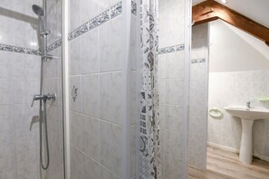A shower with a handheld showerhead, a curtain with a geometric pattern, and a sink with a green soap dish.