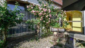 Ein rustikales Gebäude mit Backsteinfassade, einem großen Bogenfenster und einem Garten mit rosa Rosen.