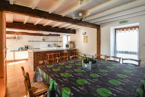 A dining area with a table covered in a black tablecloth with green patterns, wooden chairs, and a brick wall.
