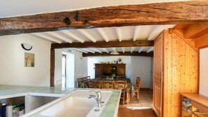 Eine Küche mit großem Spülbecken, Holzbalken, einer Essecke mit Stühlen und einem Holzkorpus.