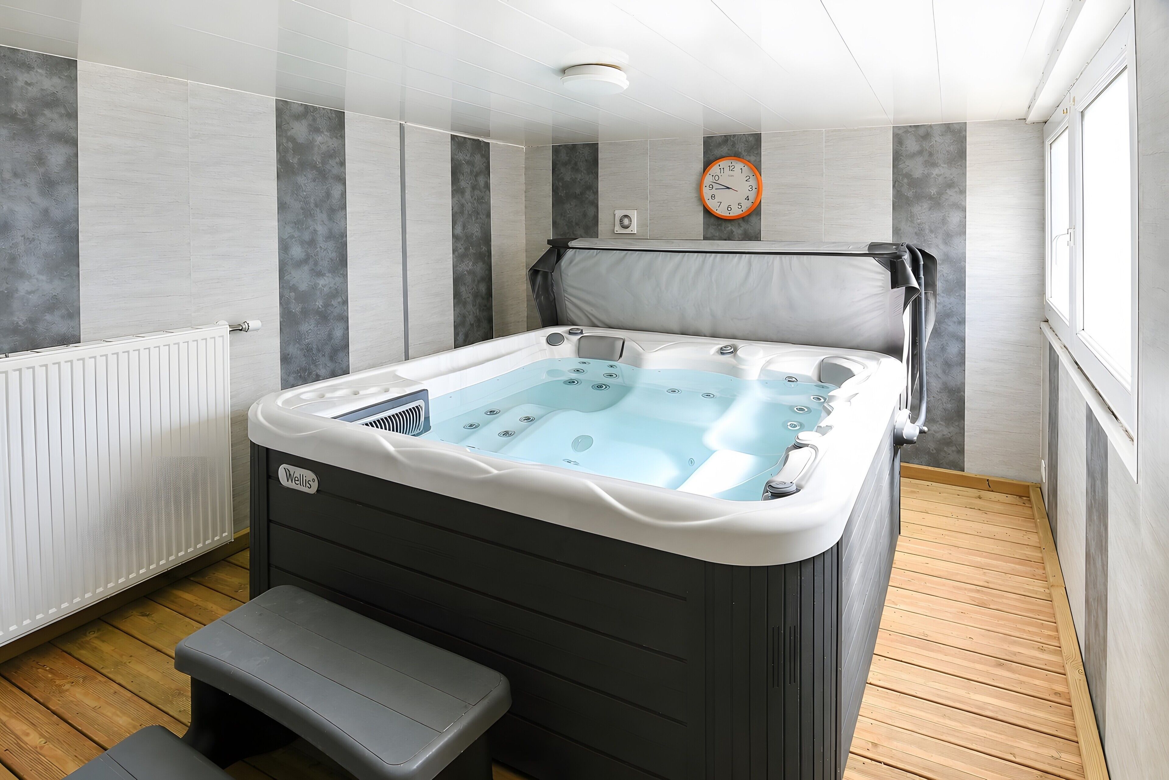 Een moderne badkamer met een bubbelbad, houten vloer, een bankje en een klok aan de muur.
