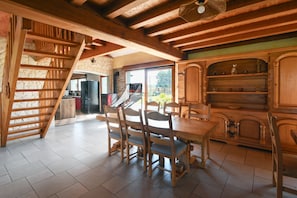A wooden dining area with a staircase, a kitchen with a stone wall, and a view through a glass door. - Holiday Home "Gîte du Tronquoy" with Private Terrace, Garden and Wi-Fi (Aix-en-Ergny)