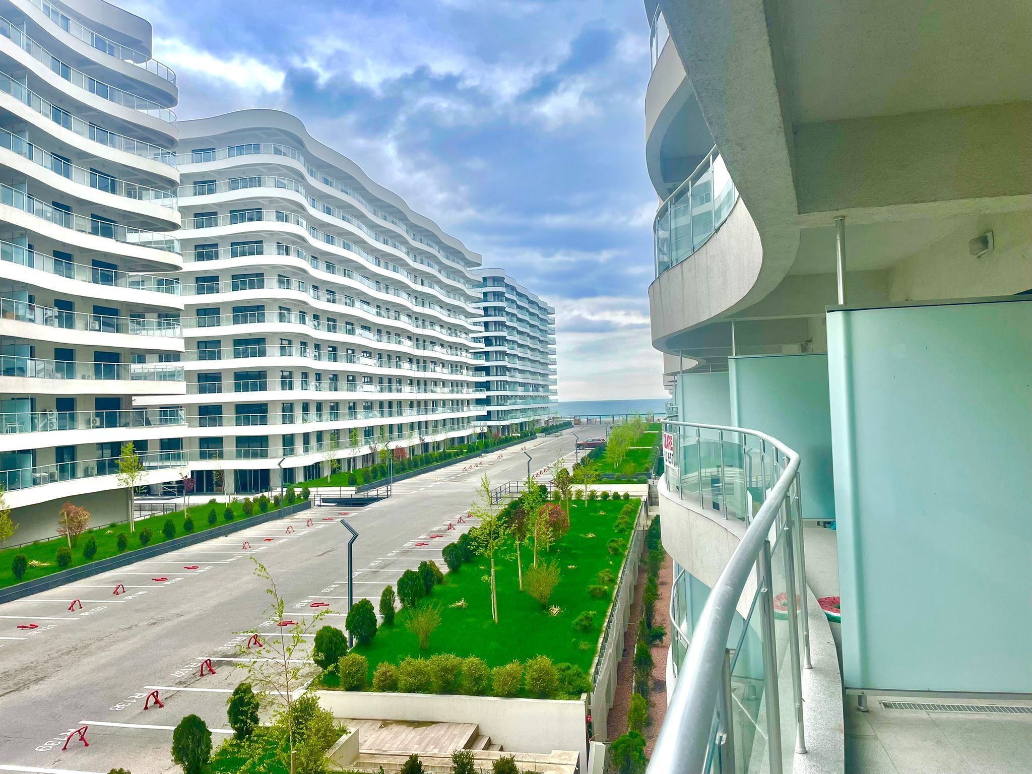 A modern multi-story hotel with a curved facade, a parking lot, and a green landscaped area.