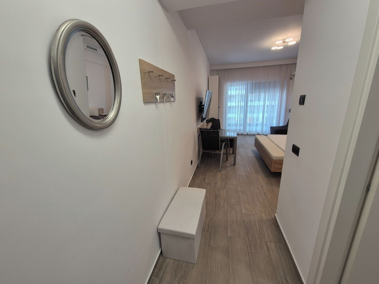 Un pasillo que conduce a un salón con un sofá, un escritorio y un espejo en la pared.