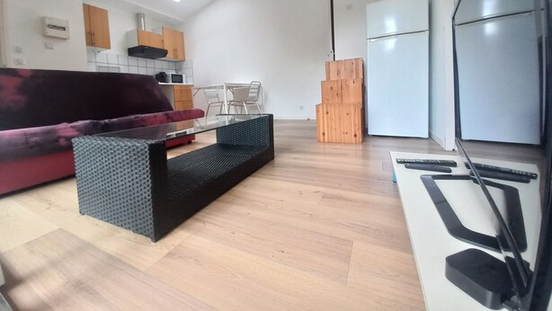 Un salon moderne avec un canapé, une table basse en verre et un coin cuisine équipé de placards et d’un réfrigérateur.
