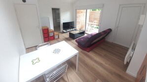 Un espace de vie compact comprenant une table à manger, un canapé, un téléviseur et une porte-fenêtre coulissante donnant sur un espace extérieur.