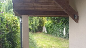 Un espace extérieur abrité, doté d’un sol en béton, entouré d’une végétation luxuriante et d’une pelouse.