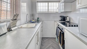 Une cuisine moderne équipée d’un évier, d’une cuisinière et d’un four, avec des meubles blancs et un sol décoré d’un motif en chevrons.