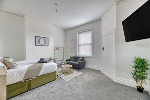 A bedroom with a bed, a sofa, a small table, a potted plant, and a window with blinds. - Glendale House by Guestz (Lytham-St-Annes)