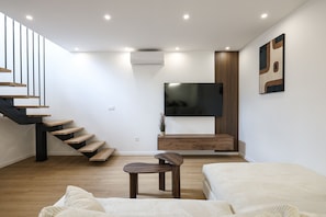 Ein modernes Wohnzimmer mit Treppe, Flachbildfernseher, Holzschrank und Sofa.