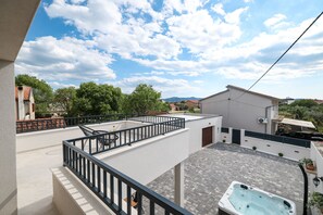 A rooftop terrace with a hot tub, outdoor seating, and a view of surrounding buildings and trees.