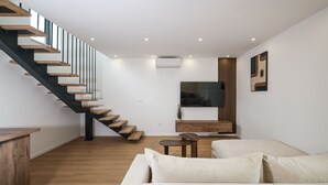 A modern living room with a wooden staircase, a flat-screen TV, a wooden cabinet, and a beige sofa. - Villa Ruzarija with jacuzzi (Sukošan)