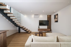 Ein modernes Wohnzimmer mit einer Holztreppe, einem Flachbildfernseher, einer Holzkabine und einem beigefarbenen Sofa.