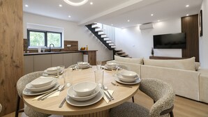 A modern dining area with a round table set for four, a staircase, and a living area with a sofa. - Villa Ruzarija with jacuzzi (Sukošan)