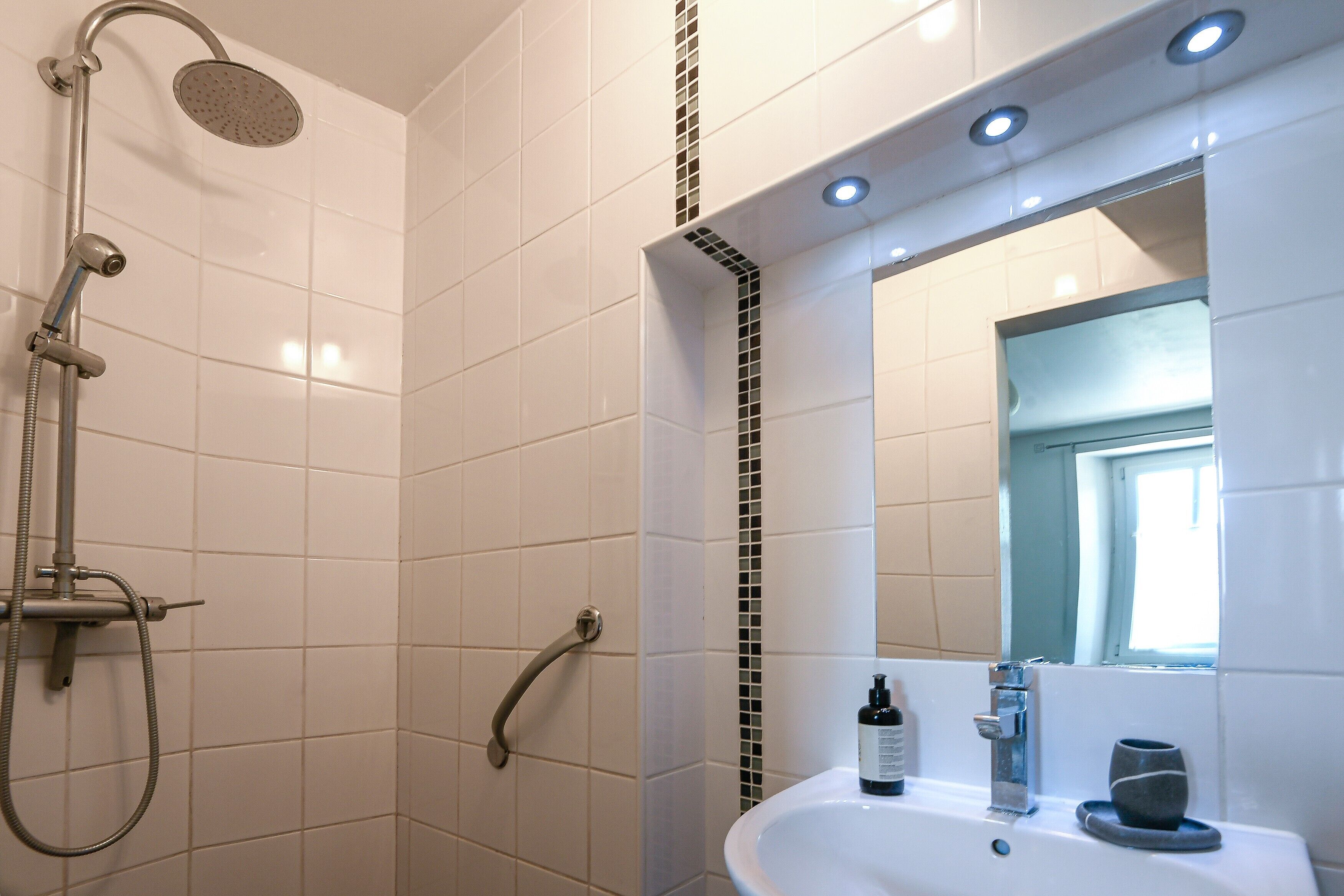 Een badkamer met een douche, wastafel, spiegel en raam.