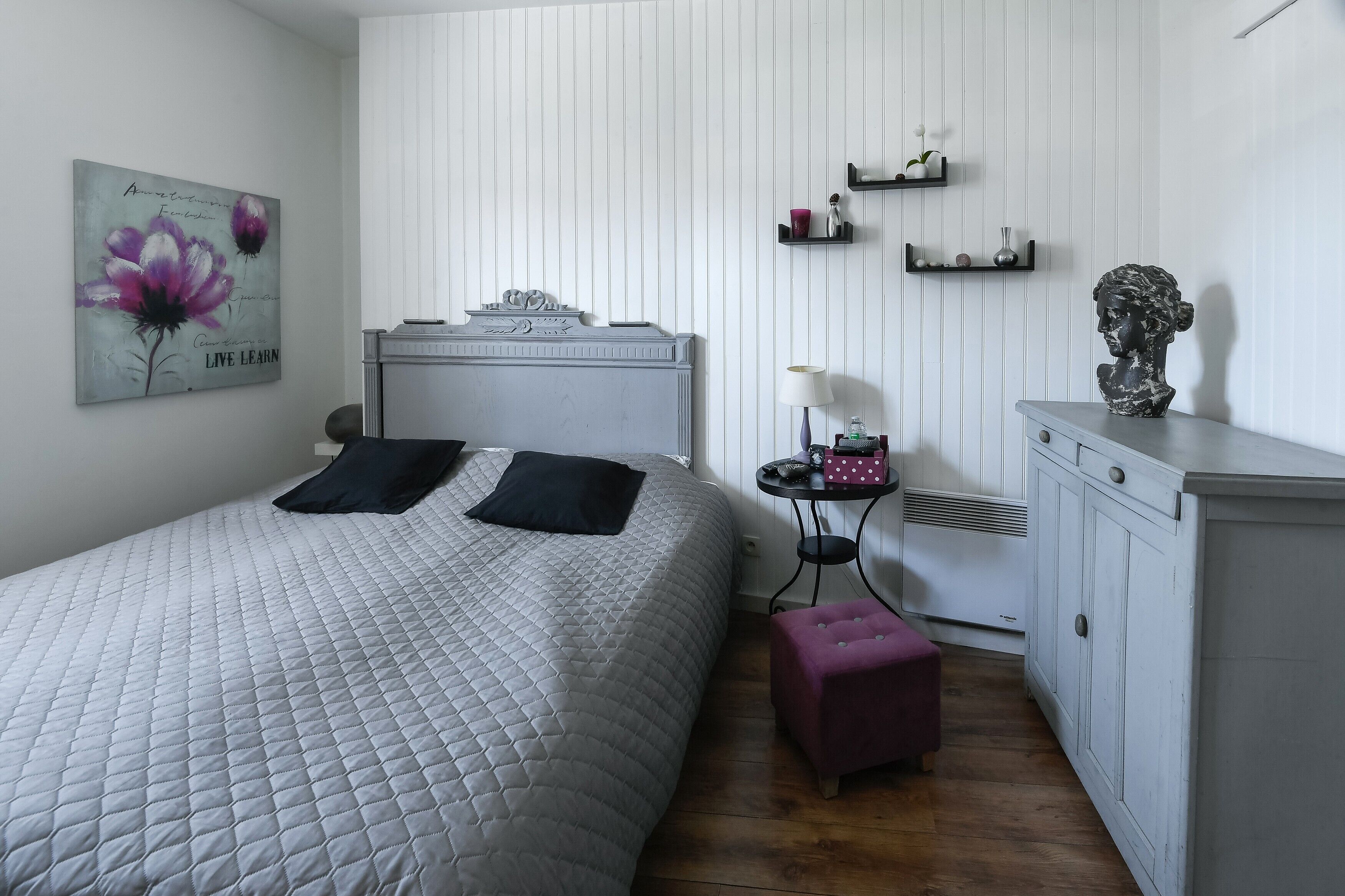 A bedroom with a bed, bedside table, lamp, and a dresser.