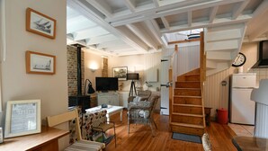 Un intérieur chaleureux avec un plancher en bois, un coin repas avec une table et des chaises, une cuisine équipée d’un réfrigérateur et un escalier menant à un niveau supérieur.