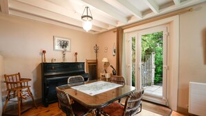 Un coin repas avec une table à plateau de verre, des chaises en osier, un piano et une vue sur un jardin extérieur, accessible par une porte vitrée.