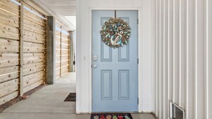 A hallway with a blue door, a wooden wall, and a metal railing. - Shell Seeker - Beachside Townhome - Just Steps from Beach (Mexico Beach)