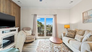 A living room with a television, sofa, and a view to the outside. - Shell Seeker - Beachside Townhome - Just Steps from Beach (Mexico Beach)